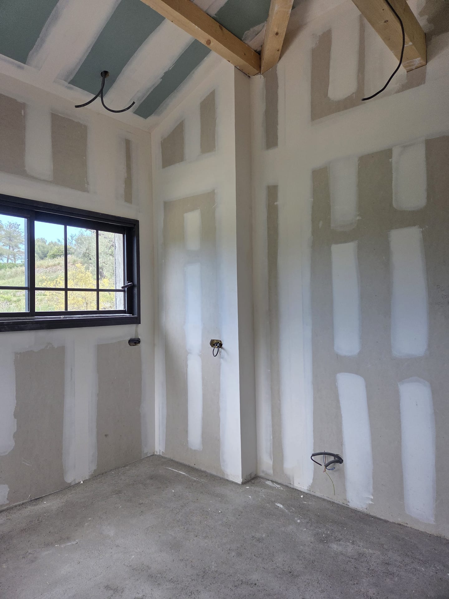 Angle de pièce avec plafond rampant en placo sous toiture, poutre apparente et fenêtre à croisillons noire dans une villa du Var