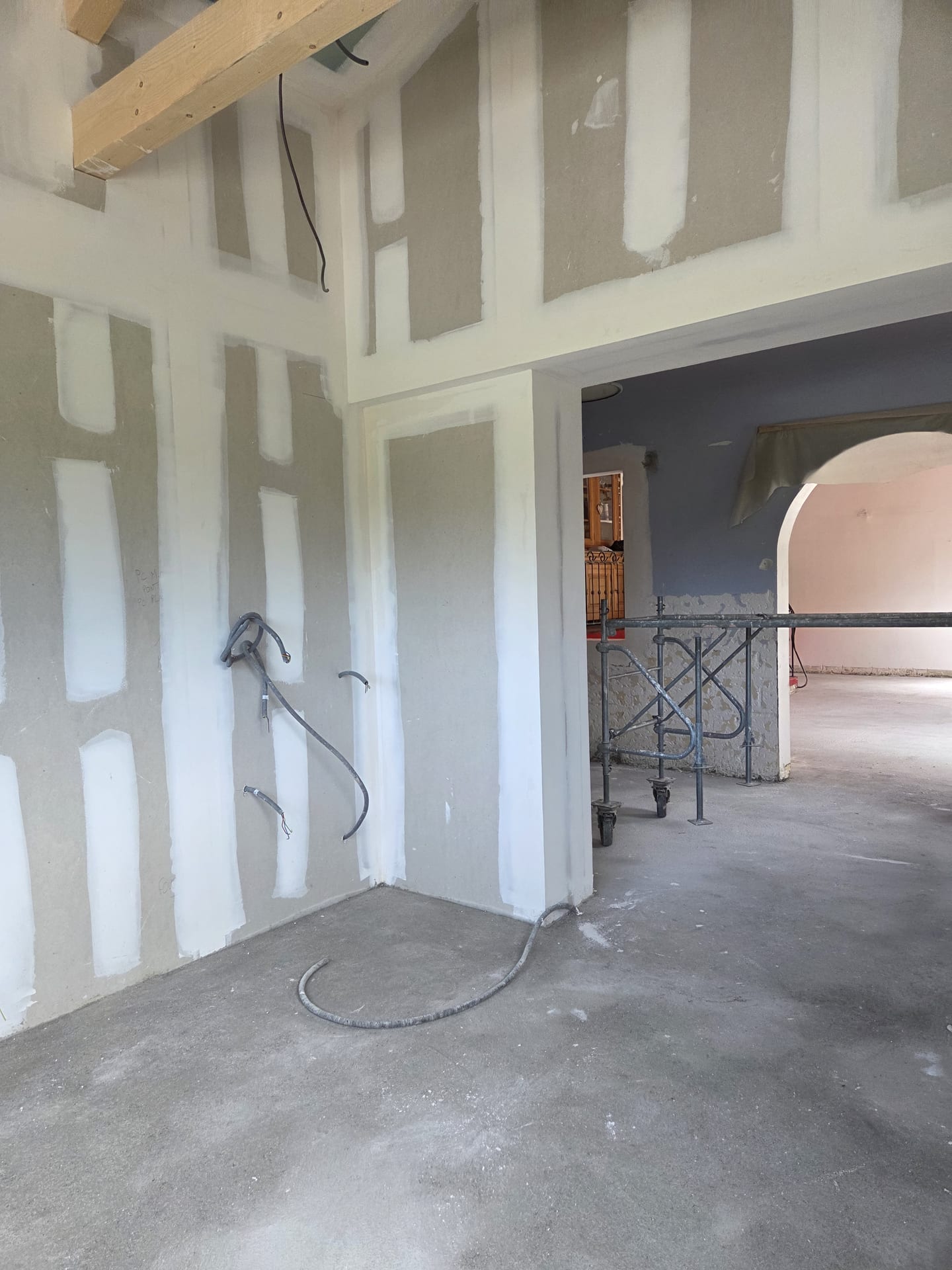 Création d'une grande ouverture en plaques de plâtre dans une villa, double hauteur sous charpente avec arche maçonnée en arrière-plan