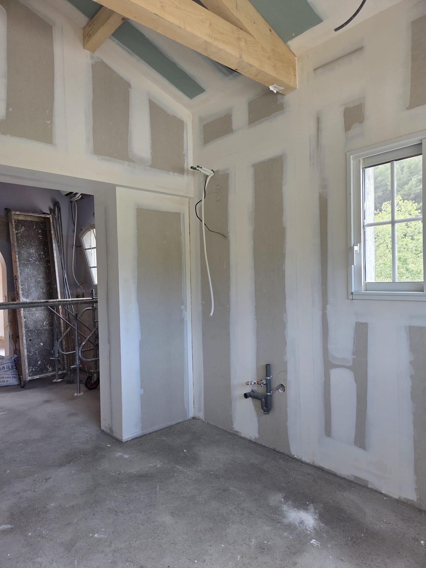 Passage et plafond rampant en plaques de plâtre dans une villa en rénovation, poutre apparente et fenêtre ouvrant sur la végétation